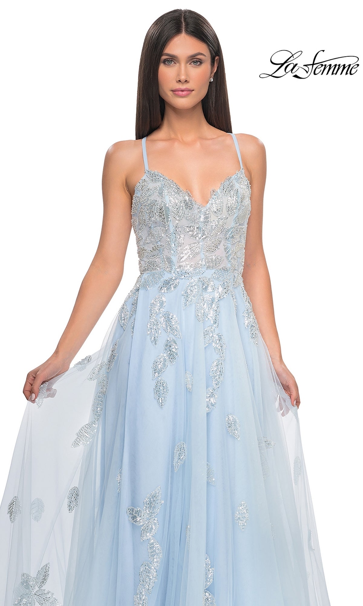 A woman models the La Femme Sequin-Embroidered Long Prom Dress 32090 in light blue, with silver leaf sequin details and spaghetti straps, against a plain white background.